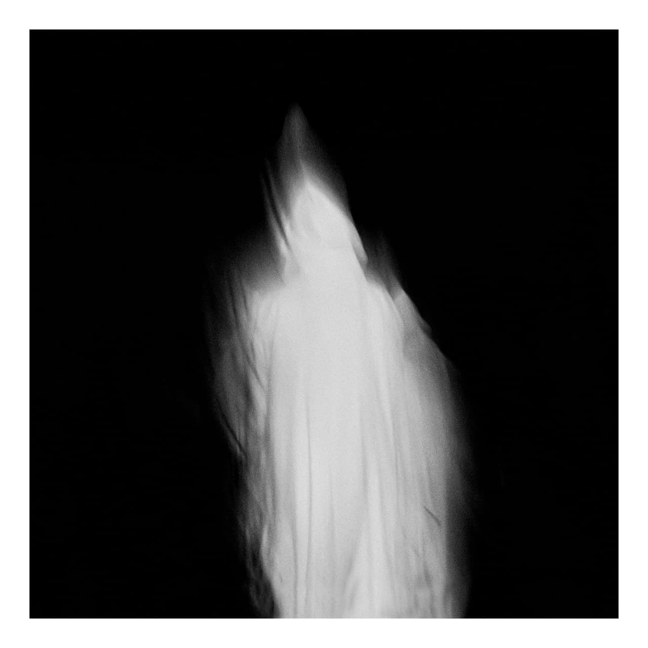 Figura con hábito blanco desdibujada por la exposición larga sobre un fondo negro, con forma de llama