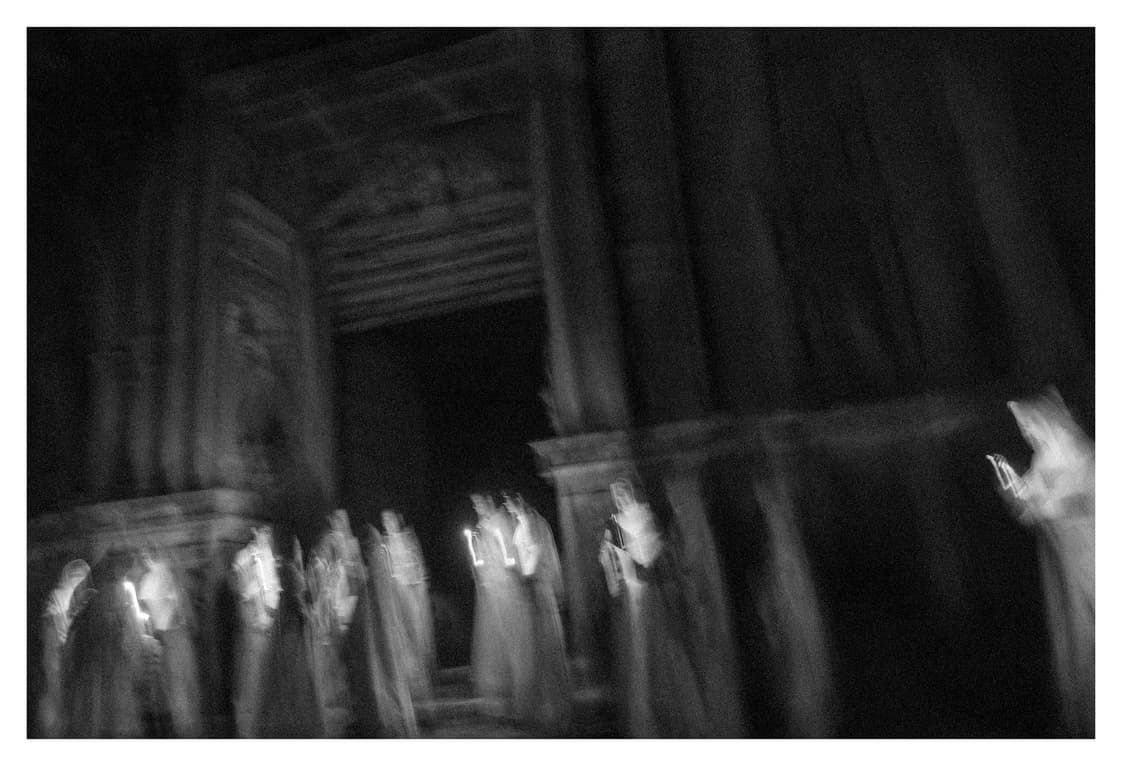 Figuras con velas cruzando ante el pórtico del monasterio, desdibujadas por la exposición larga