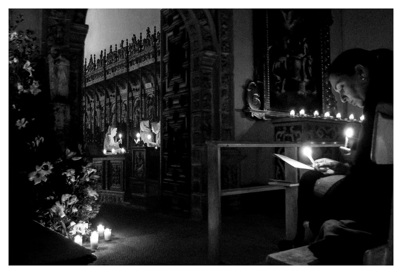 Monja leyendo a la luz de las velas en la sillería del coro, con flores blancas en primer plano
