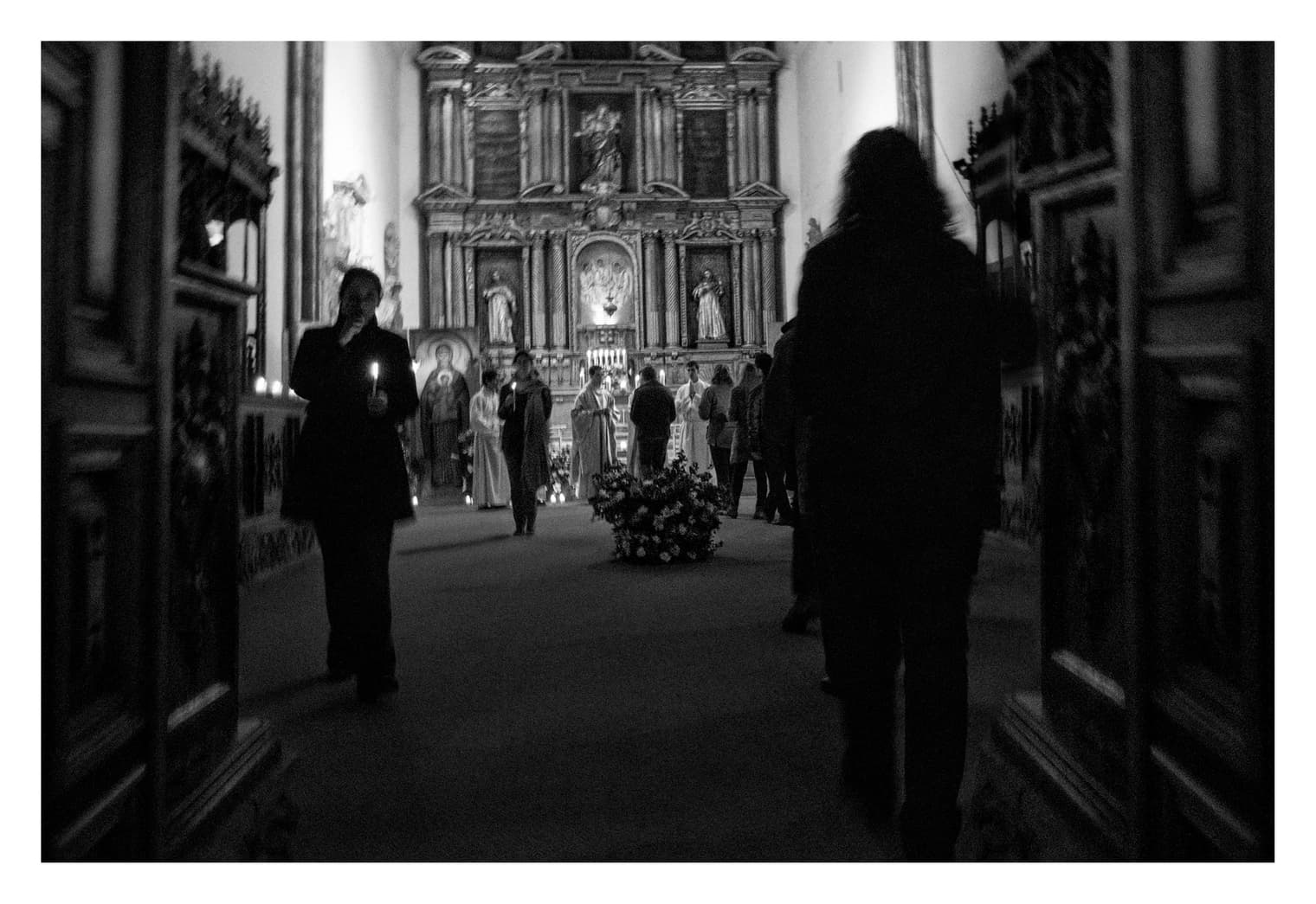 Nave del templo hacia el retablo dorado, con fieles sosteniendo velas entre la penumbra