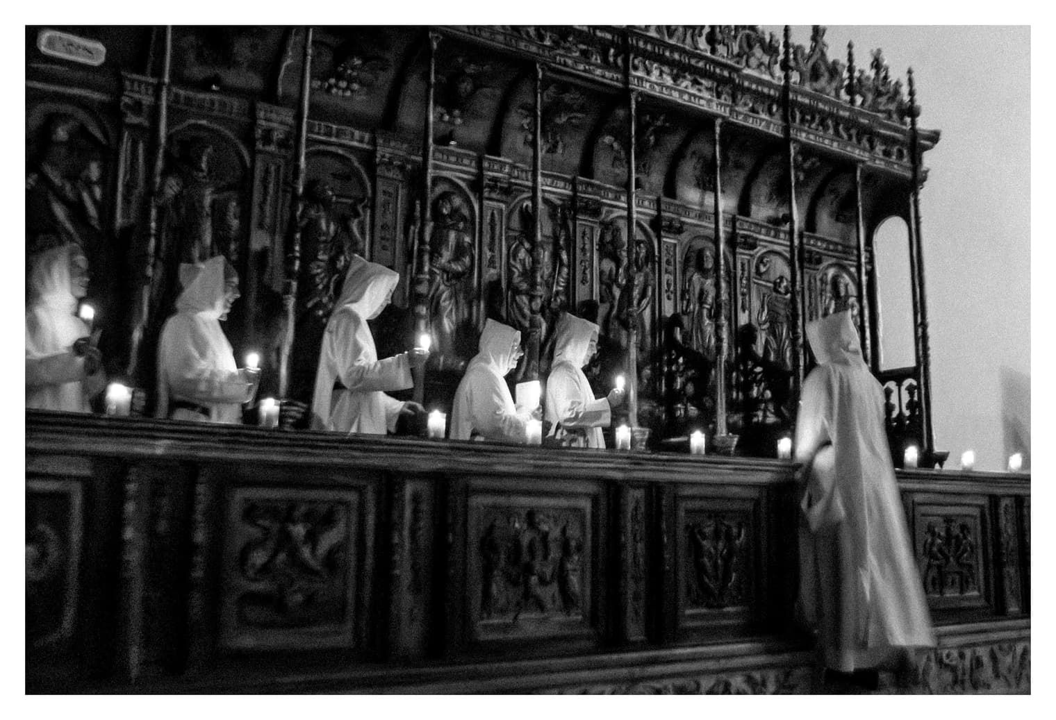 Monjas con hábito blanco y velas encendidas alineadas ante la sillería tallada del coro