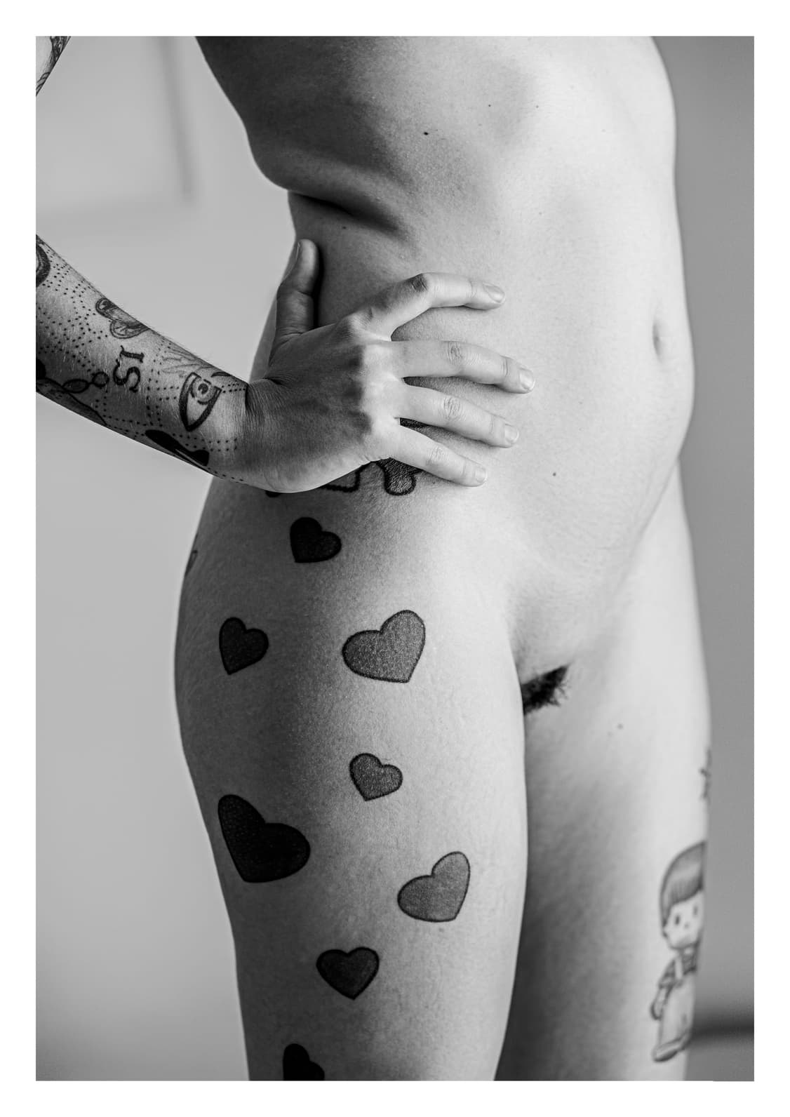Cadera y muslo desnudos con tatuajes de corazones, y una mano apoyada en el vientre