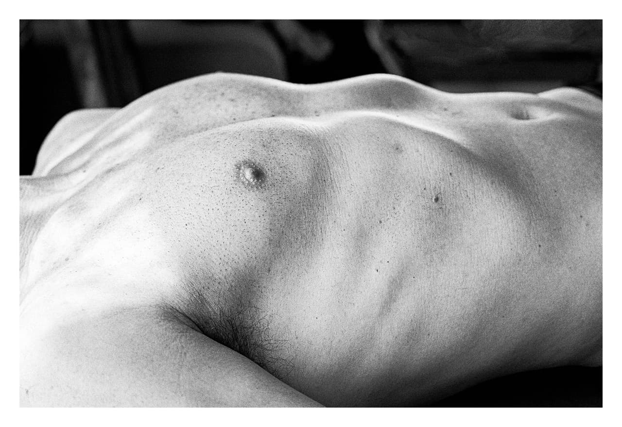 Torso desnudo tendido en horizontal, con la luz rasante marcando las costillas sobre fondo oscuro