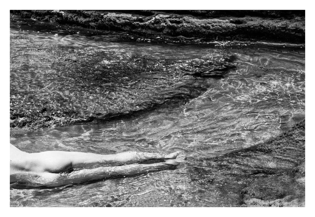 Cuerpo desnudo tendido en el agua poco profunda de un río, sobre el lecho de roca
